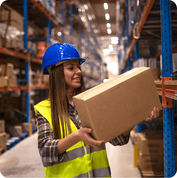 Logistics operator with a helmet and reflective vest carrying a box in a wholesale warehouse